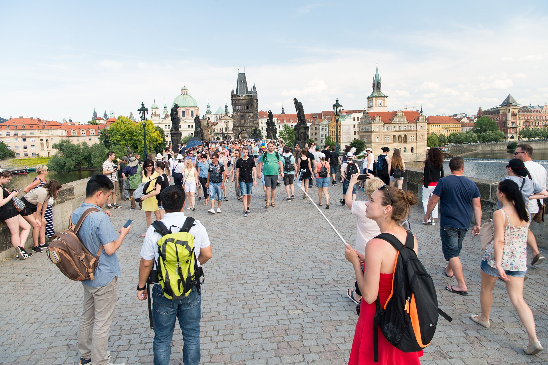 Молодые люди с рюкзаками идут по Карлову мосту в Праге, за ними – Староместская мостовая башня